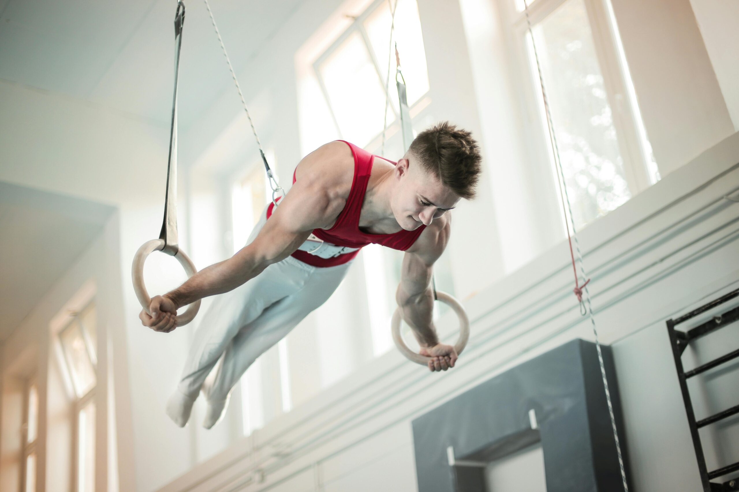 A male gymnast showcases strength and balance on rings during practice inside a gym.