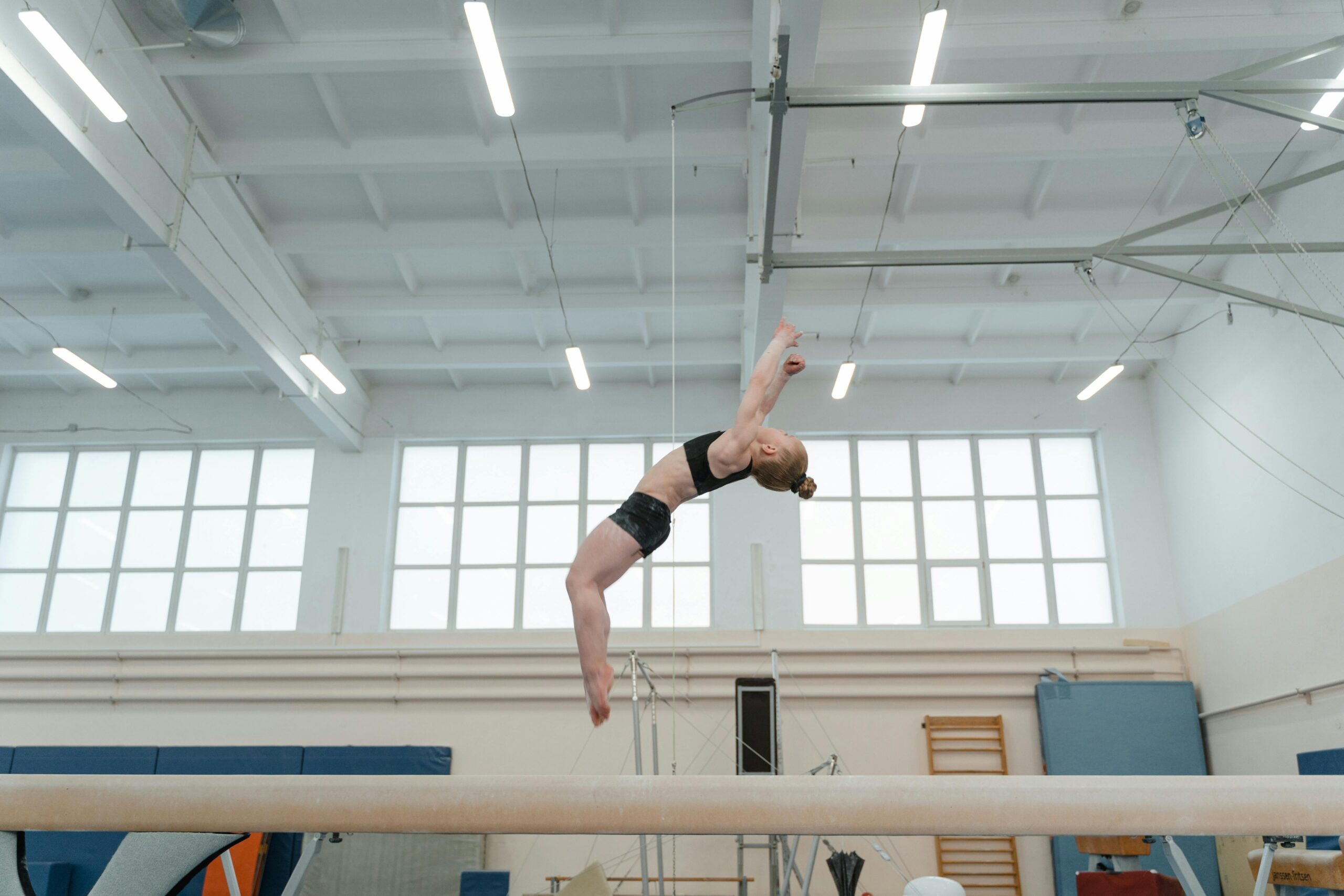 Young gymnast performs a backflip on a balance beam in an indoor gym.