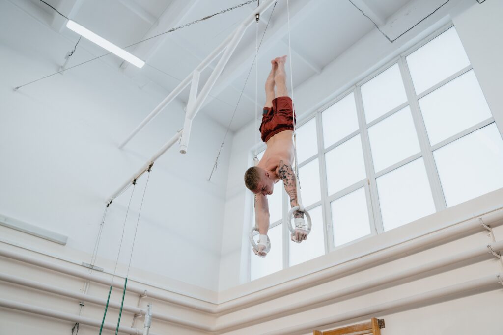 handstand Shirtless gymnast practicing upside down on rings in an indoor gym, showcasing strength and focus.